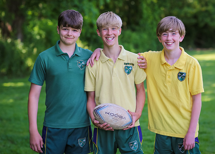 Some smiling students in their sports kit with a rugby ball