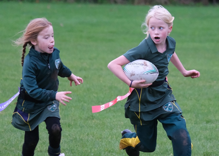 Two girls mid rugby game one with the ball