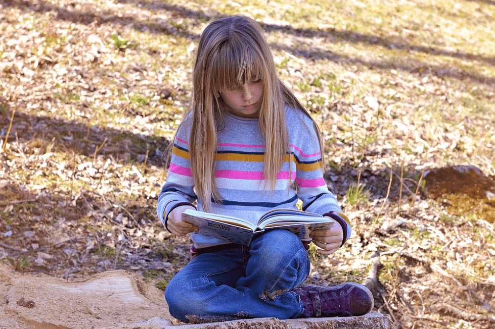 A girl sat outside with a book reading on the floor