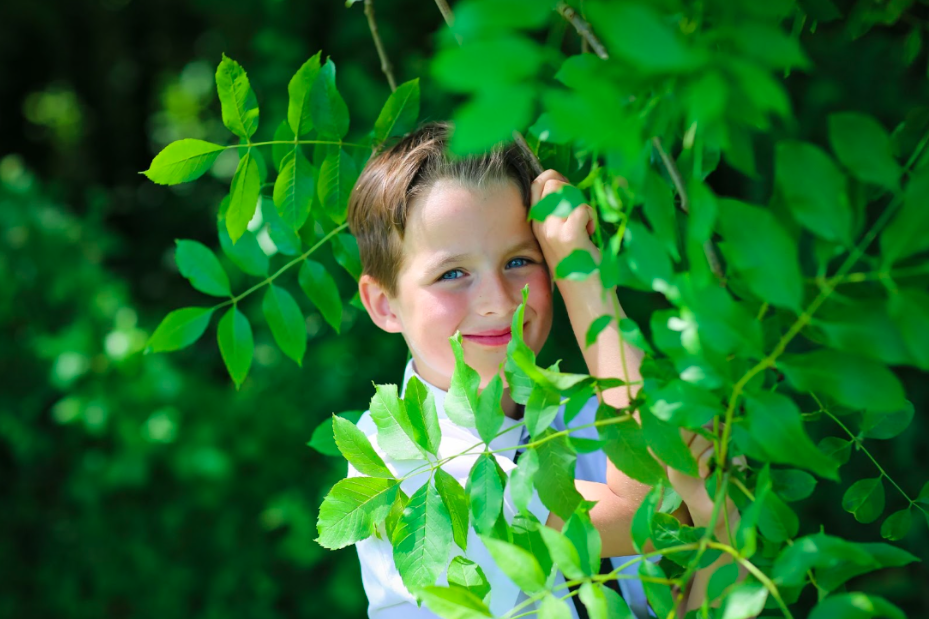 A student smiling at the camera behind outdoor green leaves
