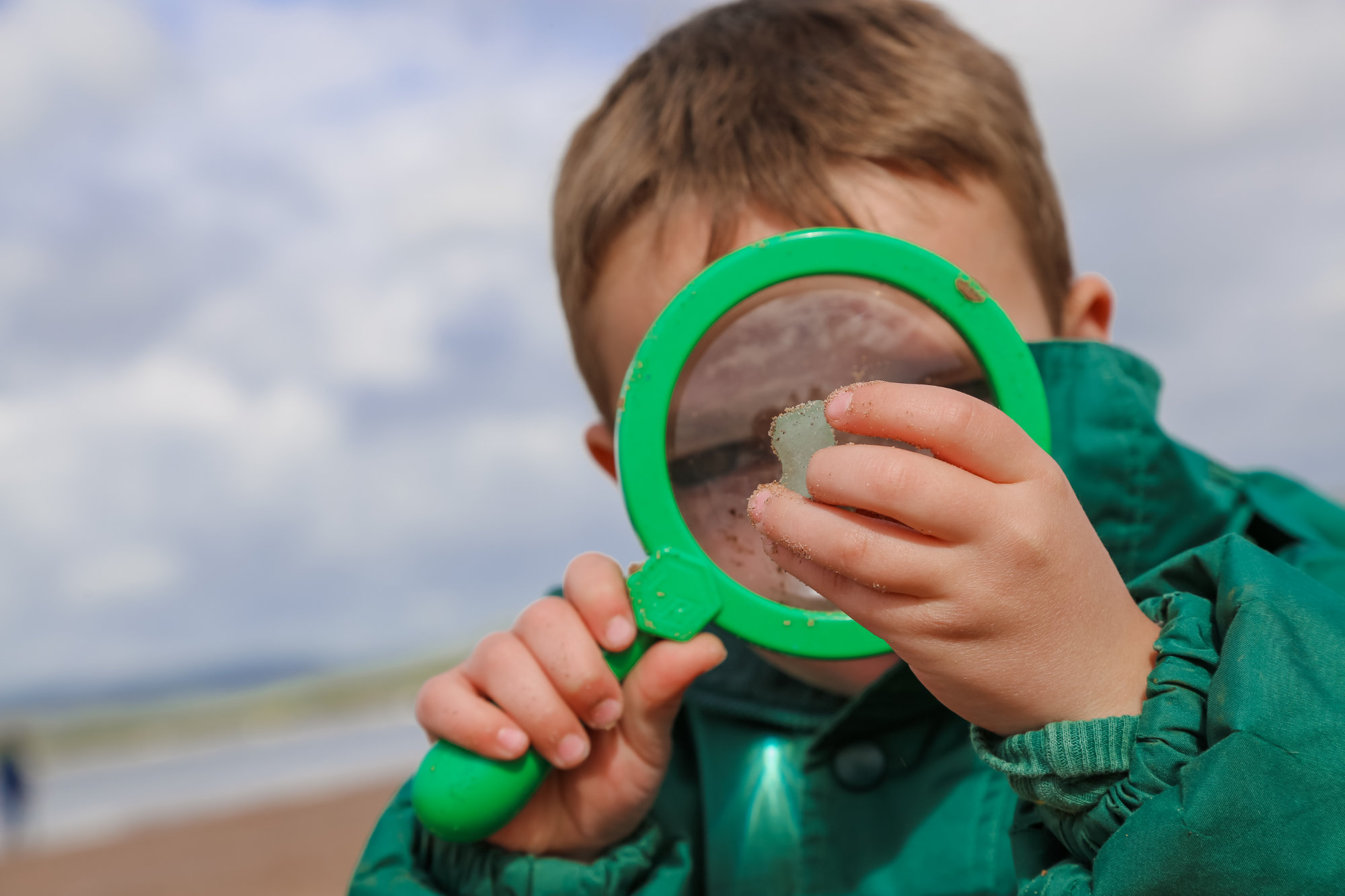 A young beach school student looking at a rock through a magnifying glass