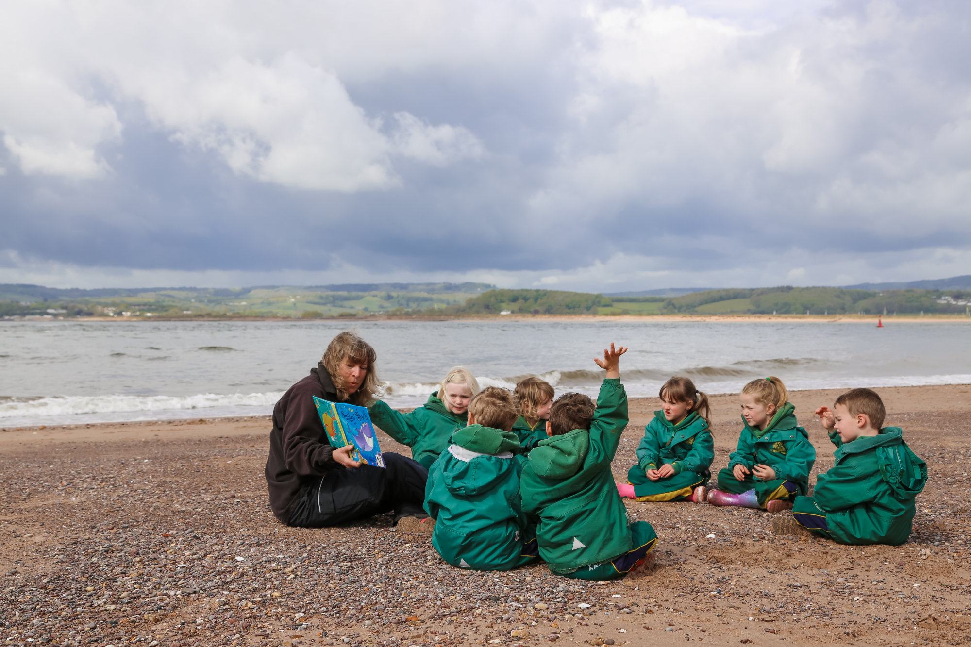 Beach school students sat in a circle on the sand with a teacher