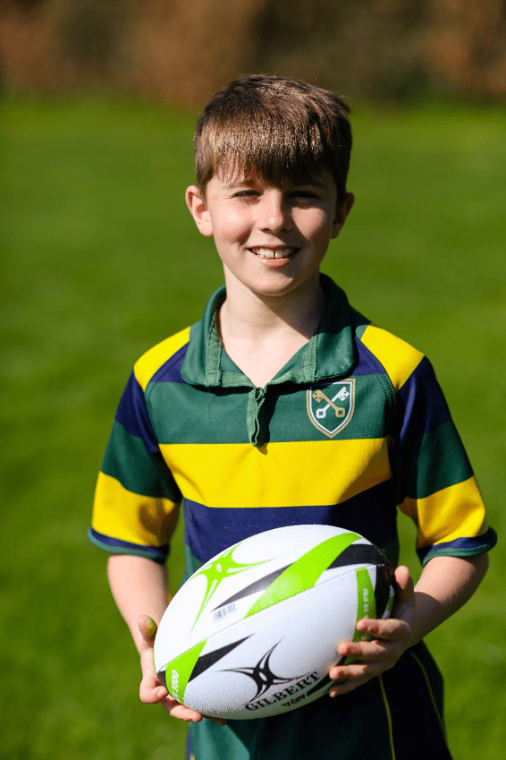 A boy stood on the pitch with a rugby ball