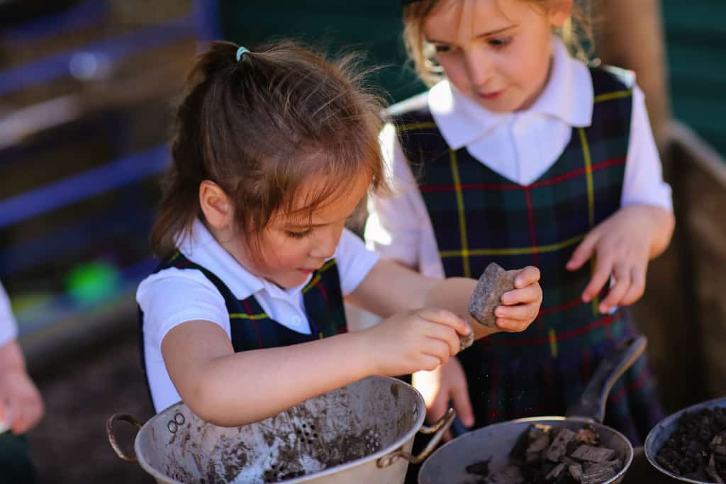 two girls playing outside school with a rock