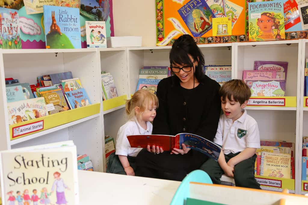 A teacher is reading a book to a girl and a boy in school