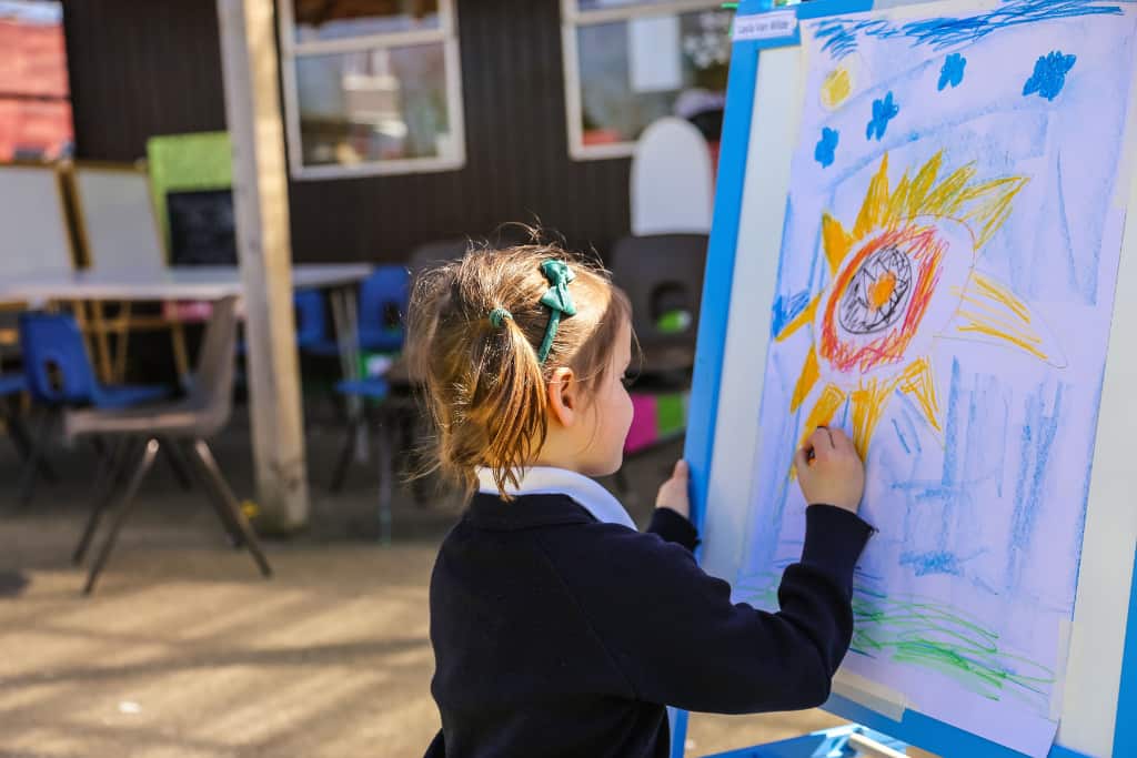 A girl outside school drawing a picture on a canvas