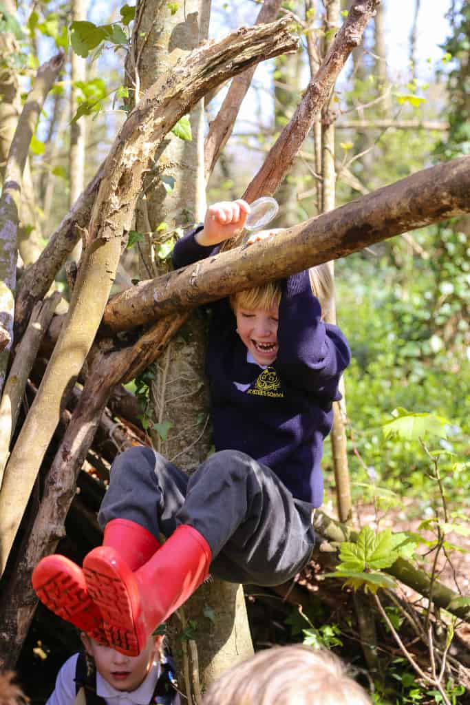 boy swinging in the tree at school with red wellies on
