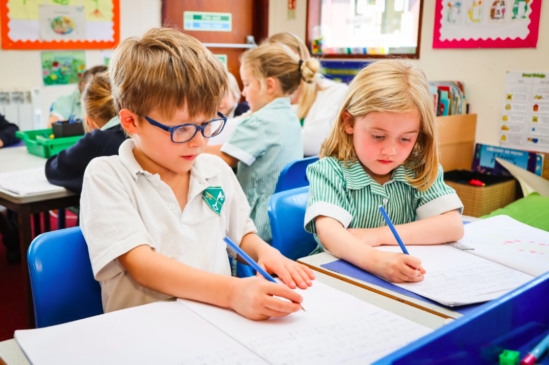 Two students sat at a desk writing