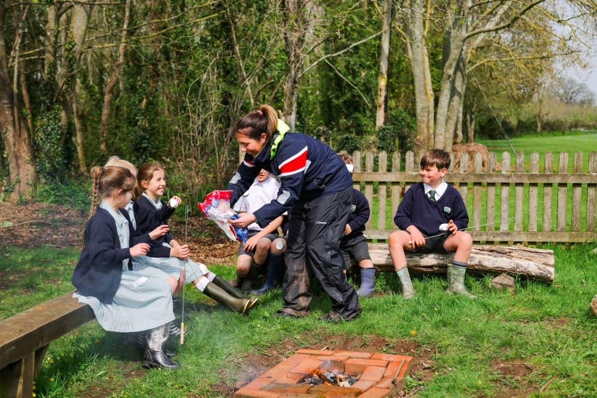 a group of students sat around an outdoor fire cooking marshmallows