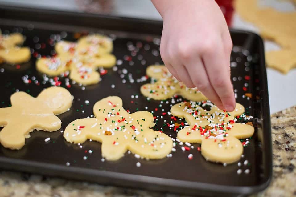 A child sprinkling a topping on to gingerbread men.