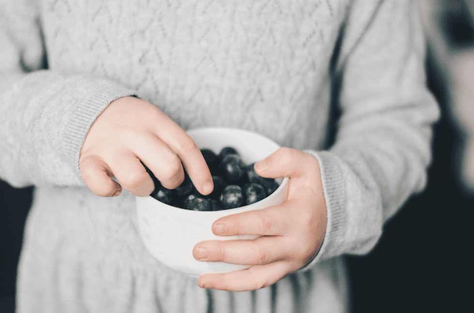 A boy holding a bowl of blueberries.