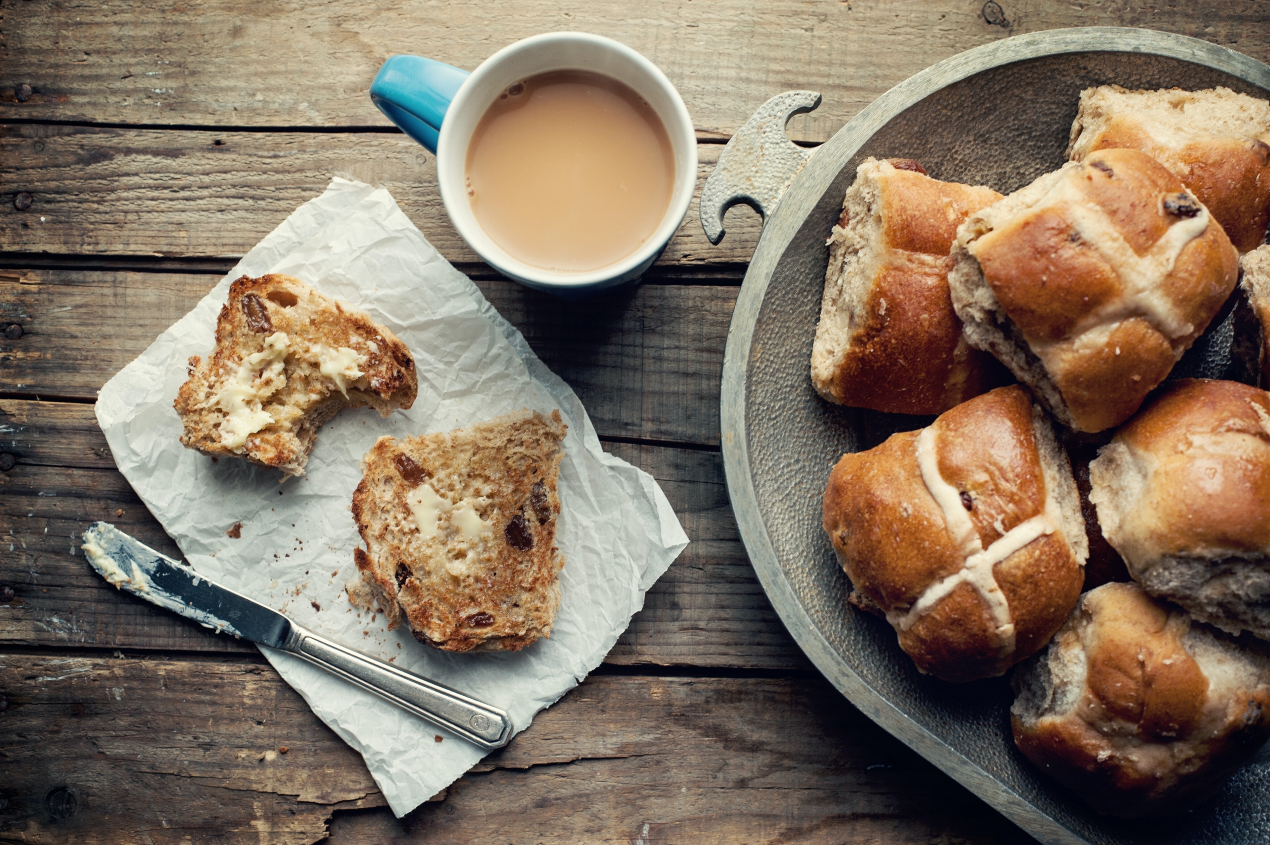 A plate of hot crossed buns next to a cup of tea