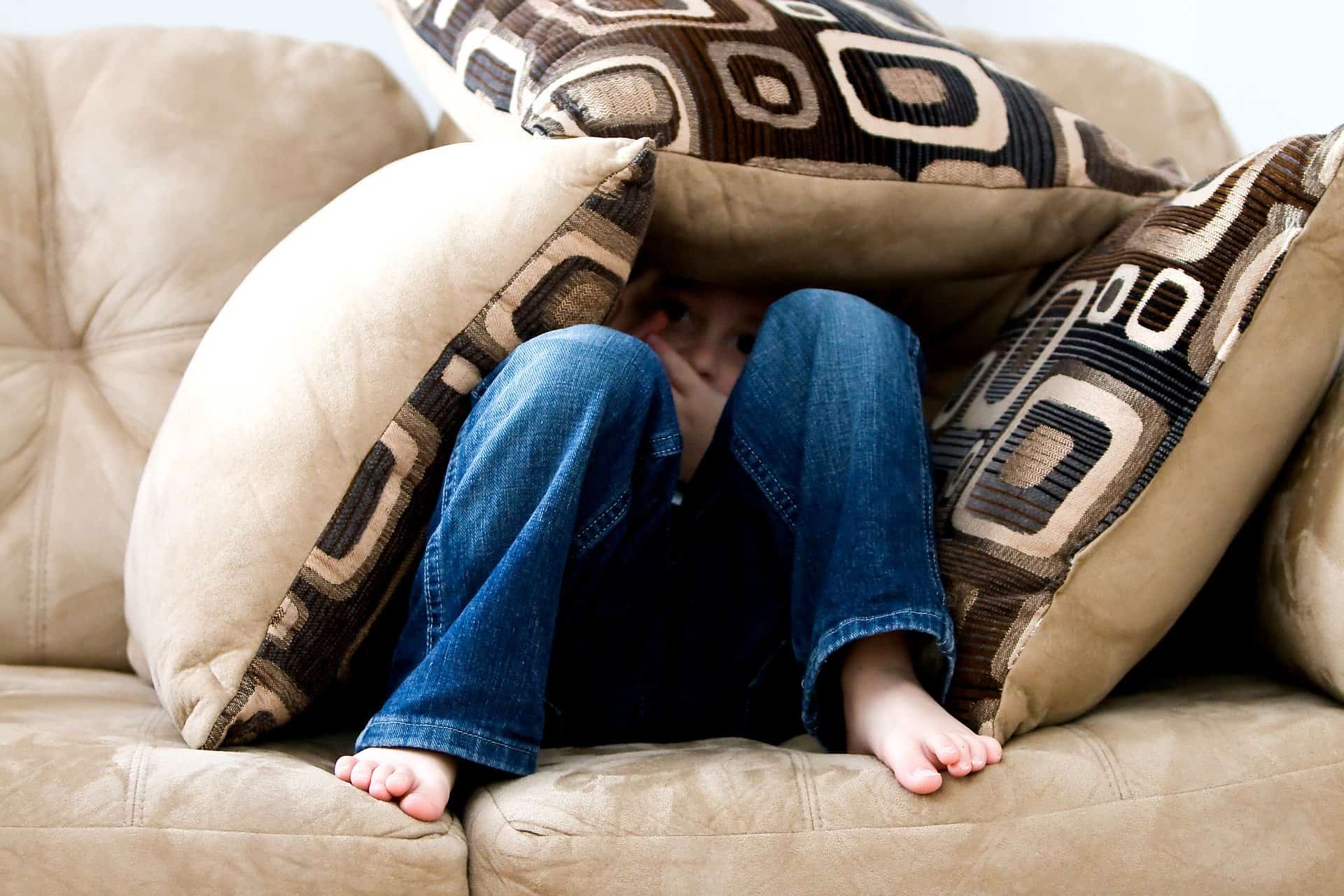 A little boy hiding underneath cushions