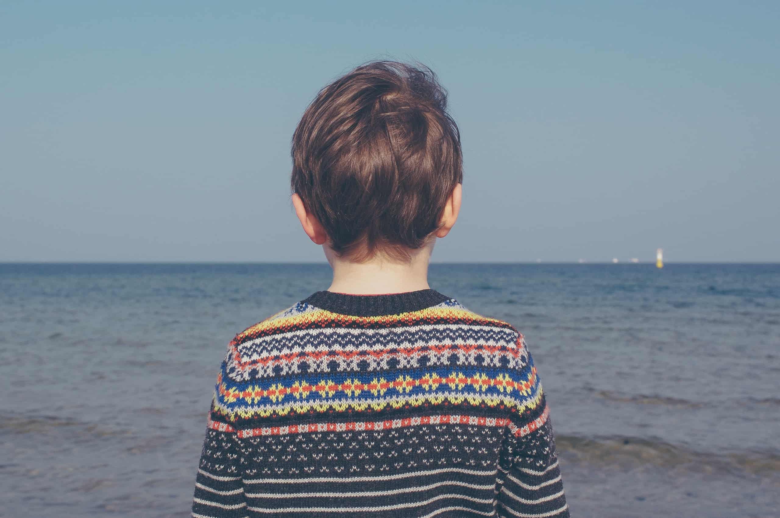 A young boy on the beach looking out to sea.