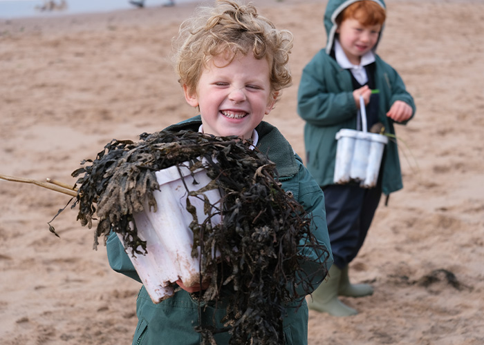 A student outside at the beach with a bucket of seaweed