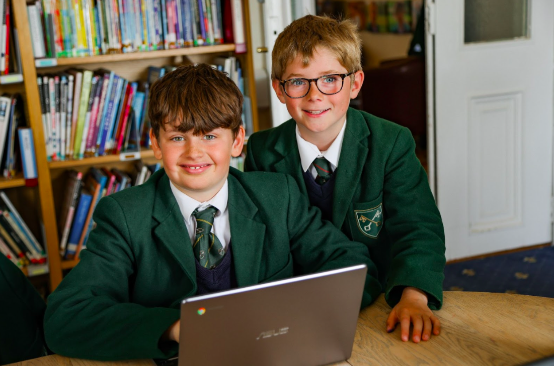 two school students working on a laptop smiling
