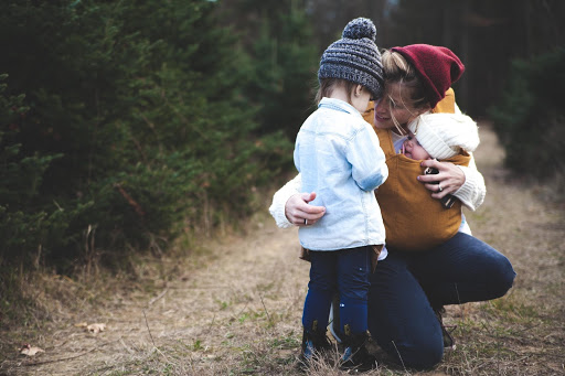 A mother crouched down holding her baby and talking to her daughter